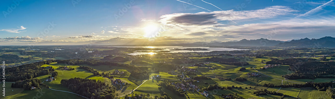 Panorama-Luftaufnahme des Chiemsees mit Sonnenaufgang hinter den Bergen.